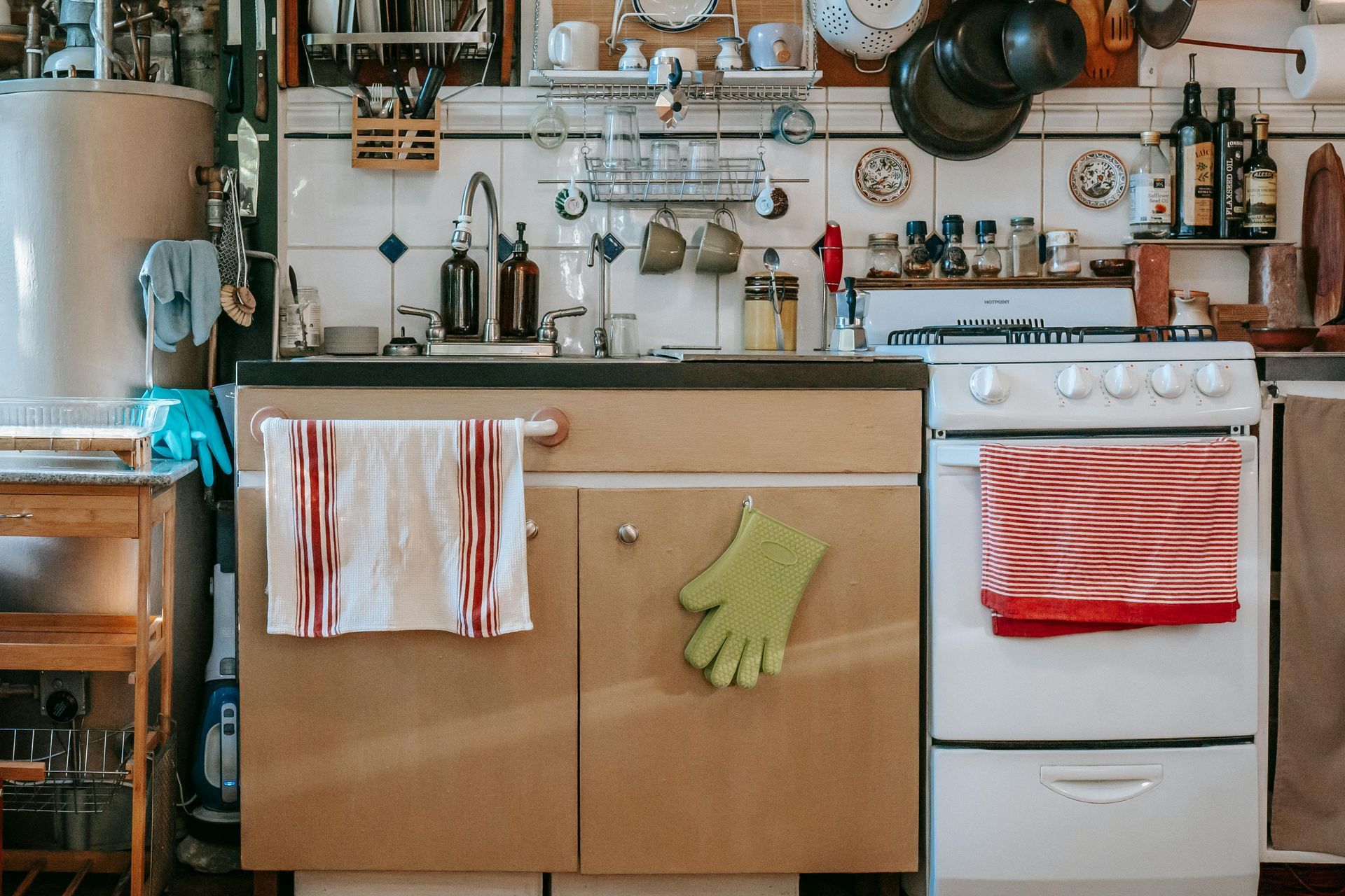 A cluttered kitchen with white stove, cabinets, sink, and various cooking utensils.
