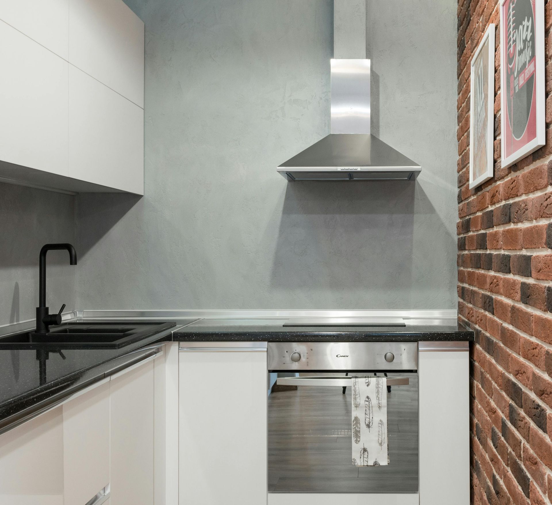 Modern kitchen with white cabinets, black countertop, stainless steel appliances, and brick wall.