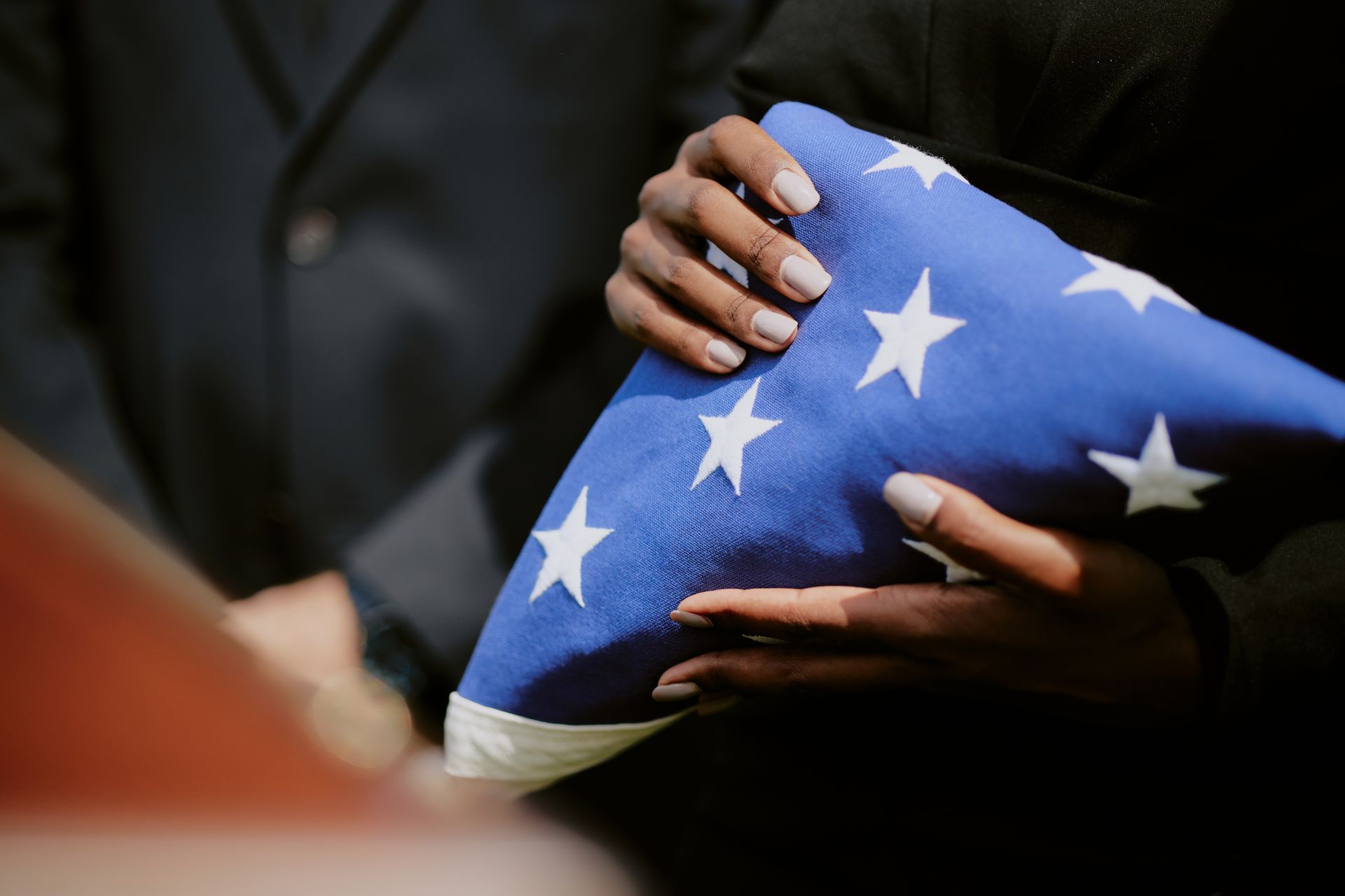 A man in white gloves is holding an american flag in front of a woman.