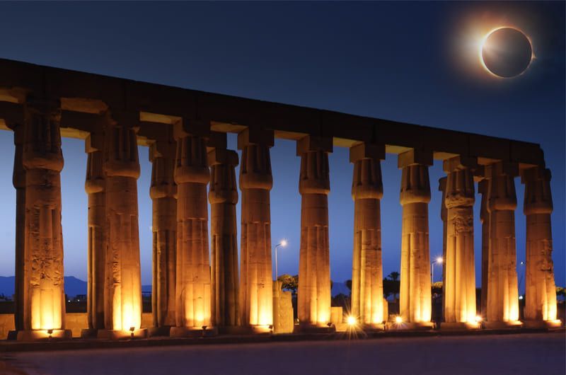 Egyptian temple lit at night with solar eclipse in the sky.
