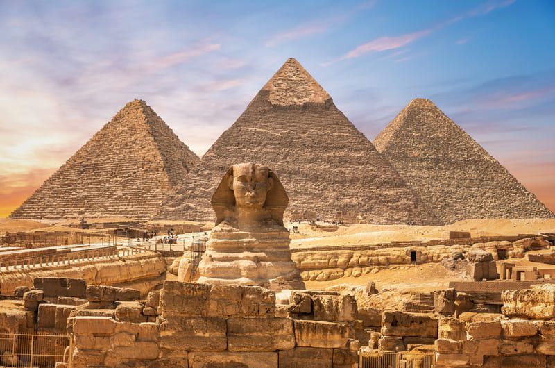 Pyramids of Giza with the Sphinx in the foreground under a colorful sunset sky.