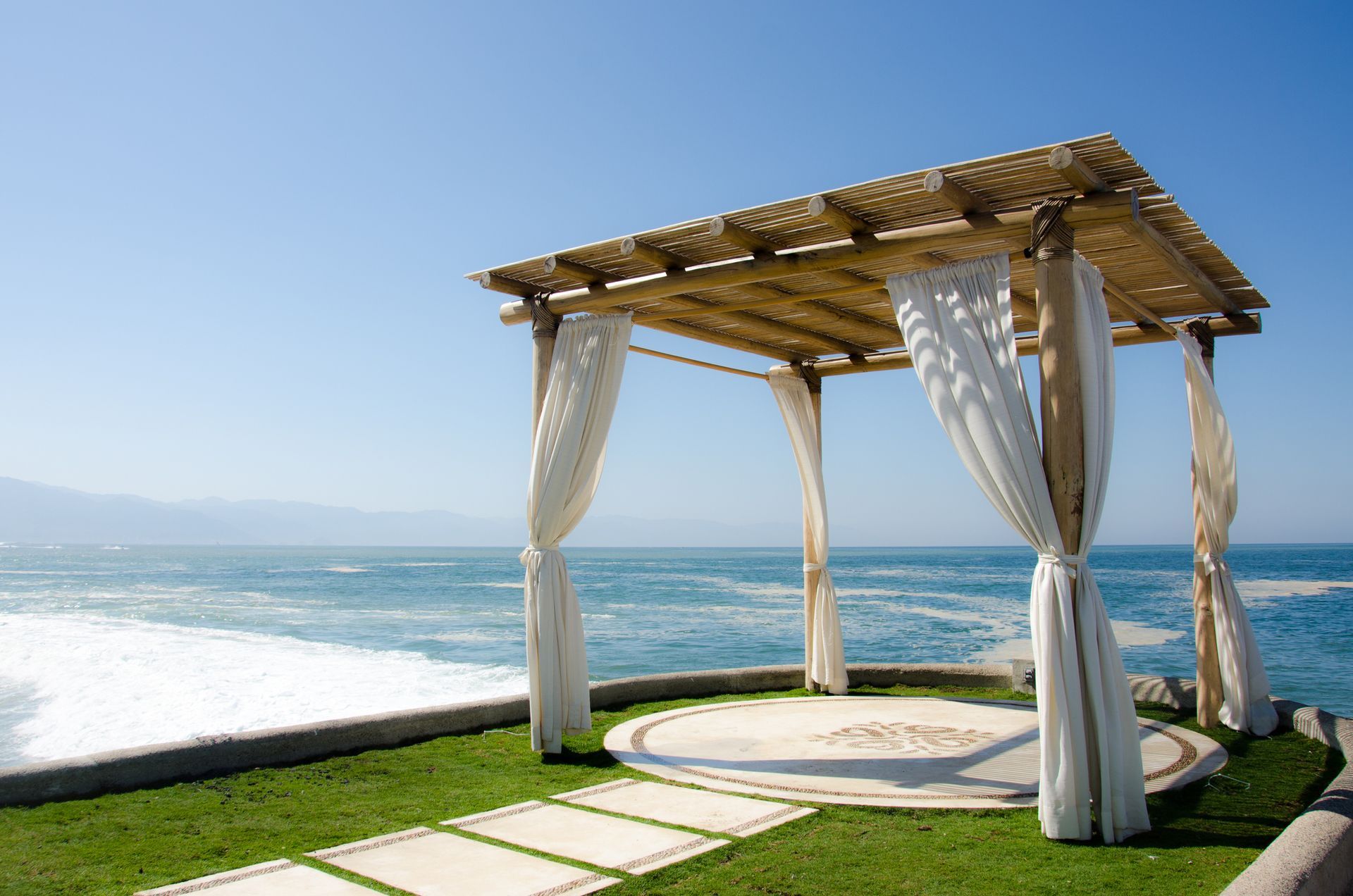 A gazebo with white curtains overlooking the ocean