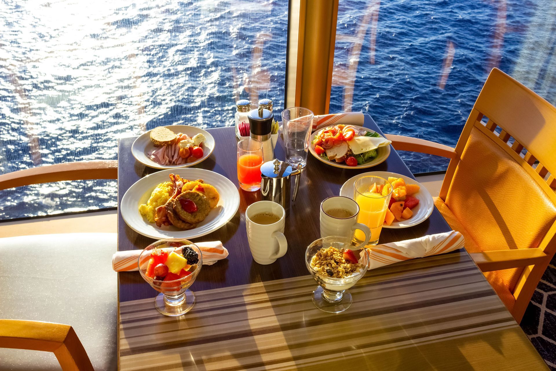 A table topped with plates of food and drinks with a view of the ocean.