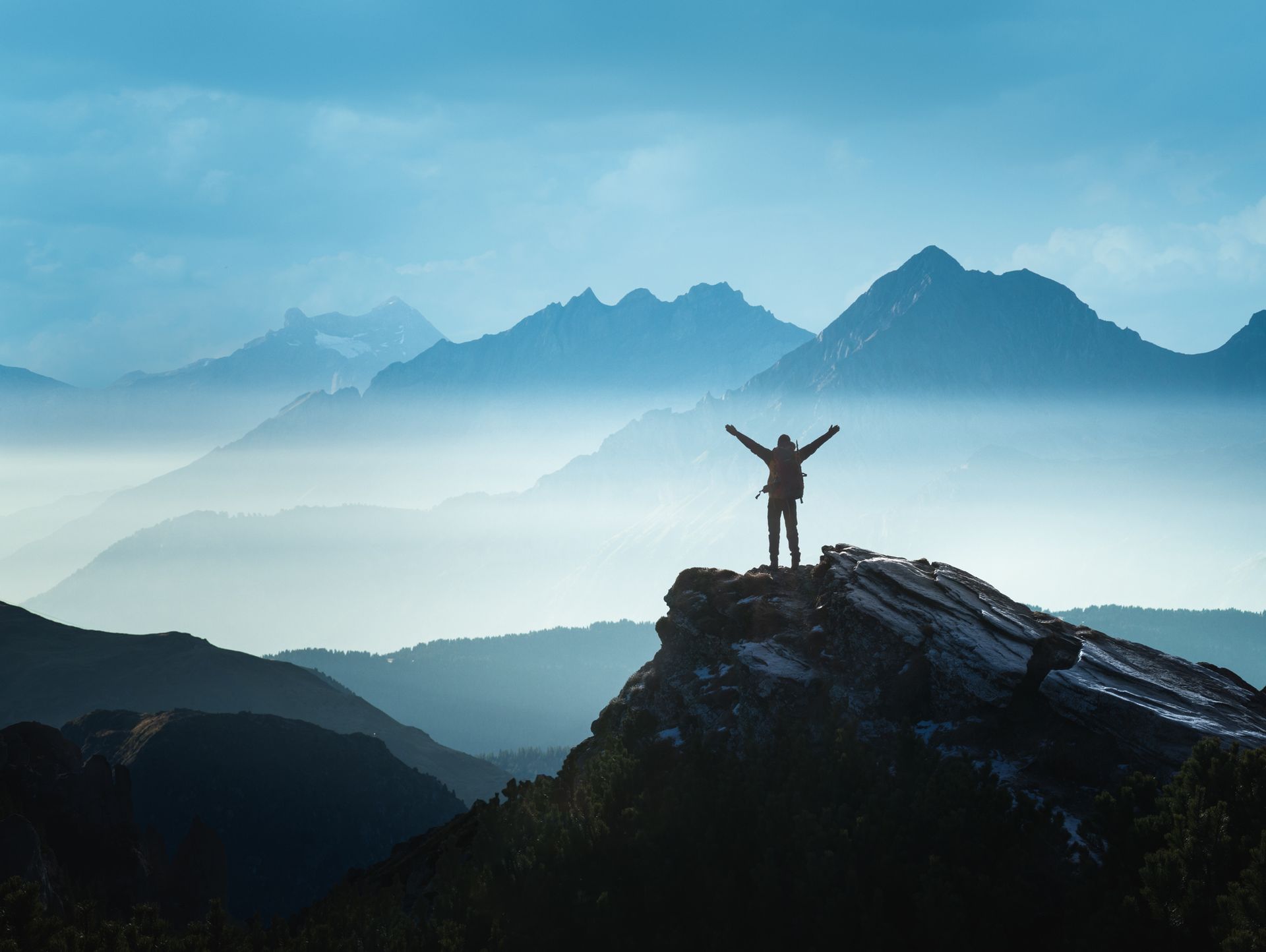 Person with arms raised on mountain peak, overlooking misty mountain range.