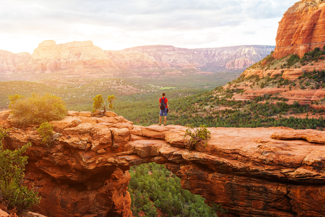 A man is standing on top of a cliff overlooking a canyon.