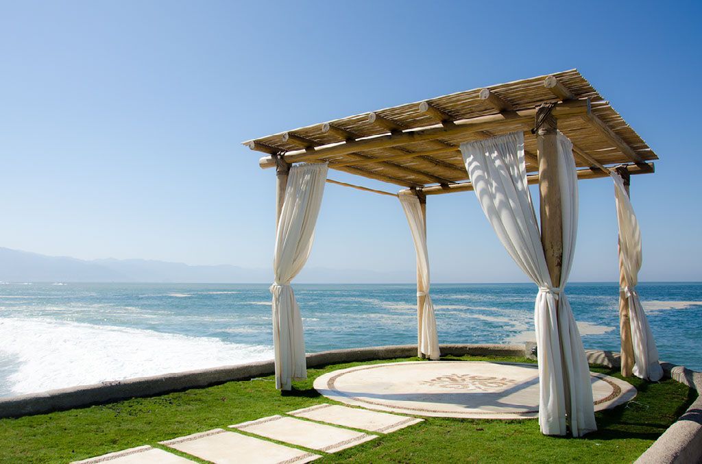 A gazebo with white curtains overlooking the ocean