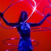 Woman with arms raised, surrounded by glowing blue hoops against a red background.