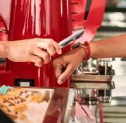 Person scans watch to pay at a red food serving station. A buffet with food items is in the foreground.