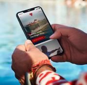 Hands holding phone showing The Virgin Boy app by a pool.