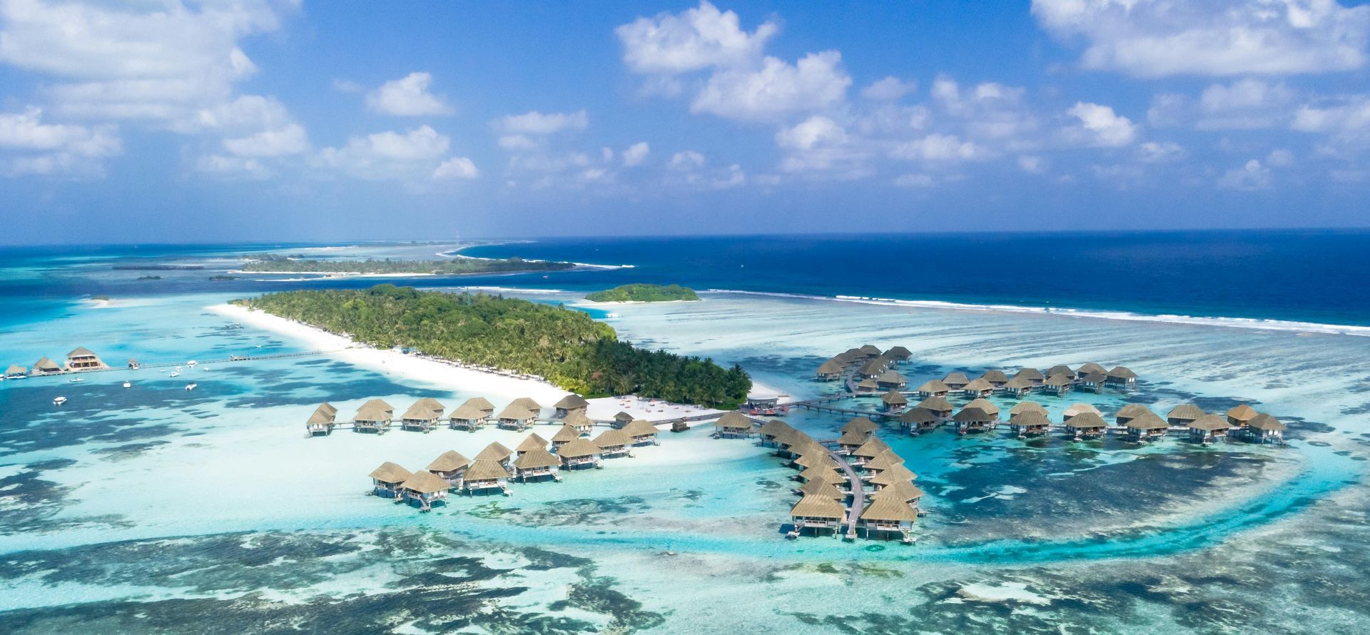 Tropical island resort with overwater bungalows, lush greenery, and turquoise waters under a bright blue sky.