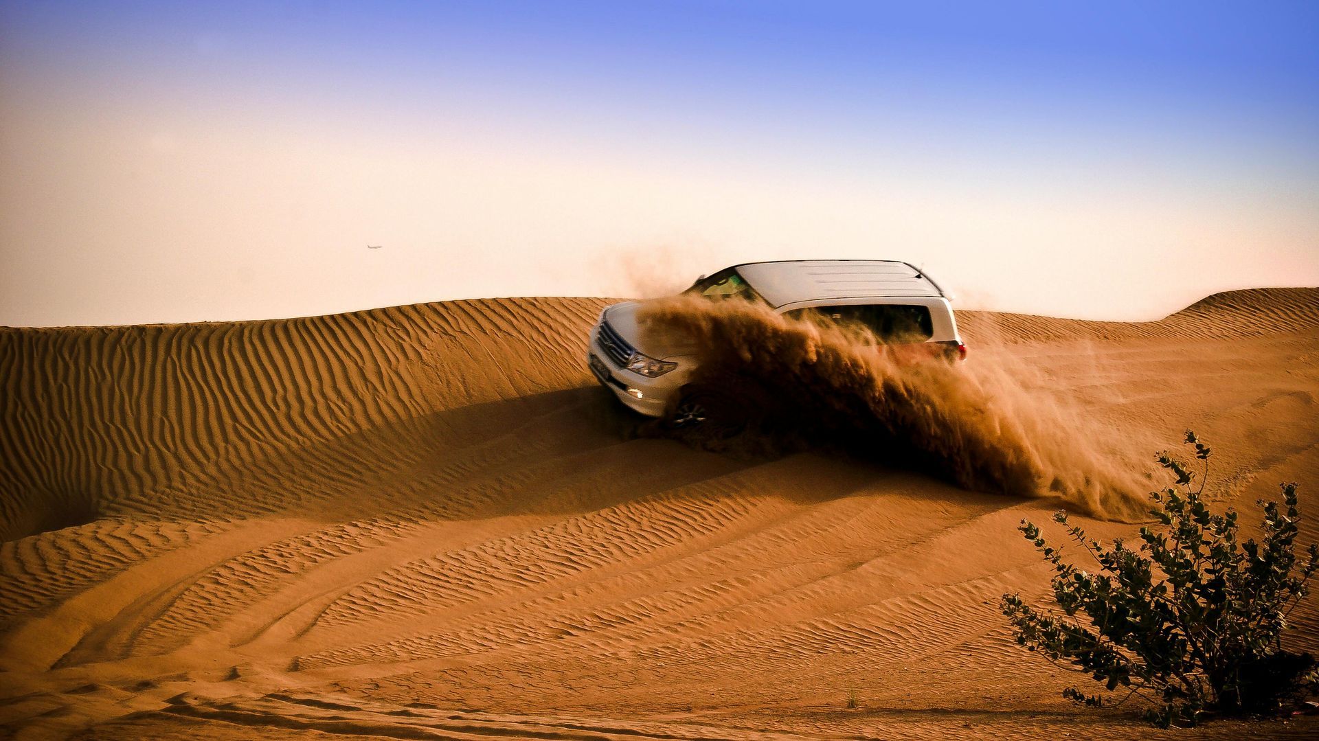 White SUV driving through a desert, kicking up sand.