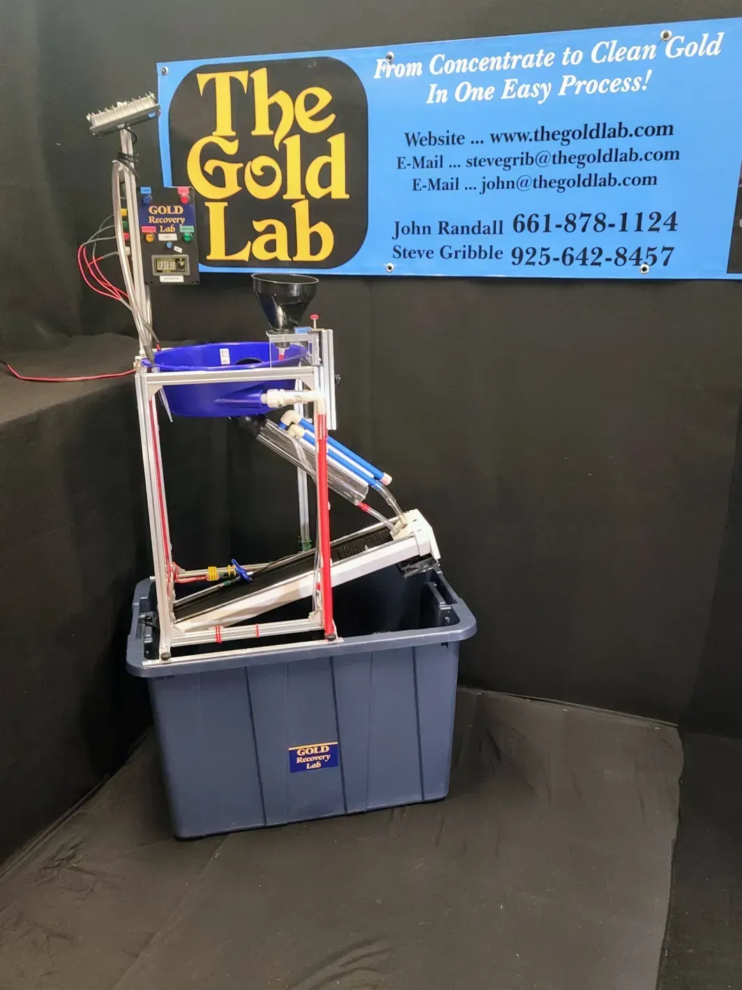 Gold Lab jewelry melting machine beside a blue bin and sign in a black booth