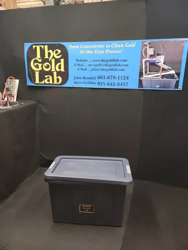 Gold Lab jewelry melting machine beside a blue bin and sign in a black booth