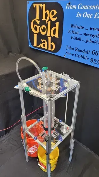 Small gold processing machine with pipes and buckets beside a “The Gold Lab” sign.