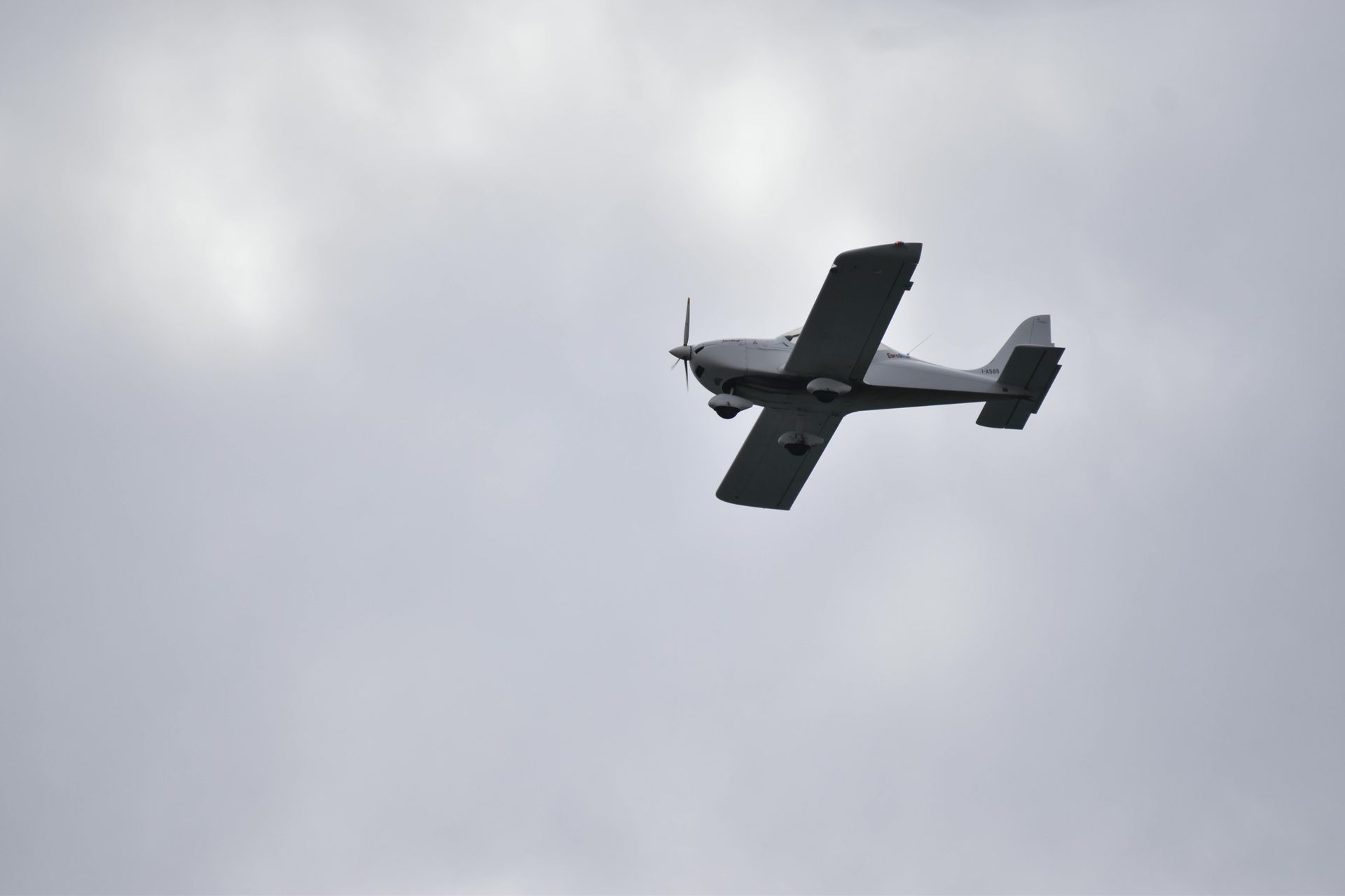 Small gray airplane flying in a cloudy sky.