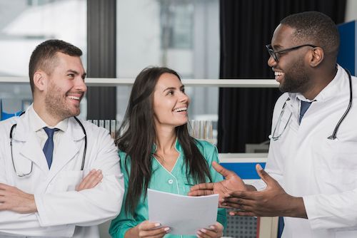 Three medical professionals smiling and conversing, in a medical office.