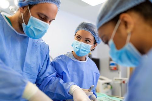 Three medical professionals in blue surgical attire attending to a patient in an operating room.