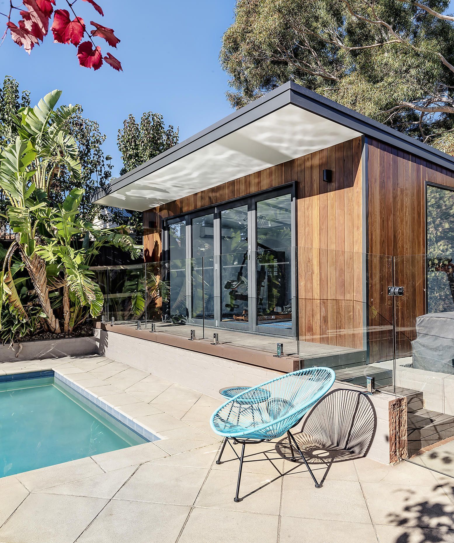 Modern glass-and-wood poolside home with patio chairs and a swimming pool