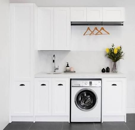 White laundry room with cabinets, sink, washing machine, hanging rack, and flowers on a counter