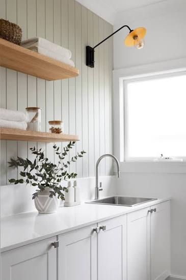 Bright white kitchen with open shelves, potted plant, sink, and a window above the counter.