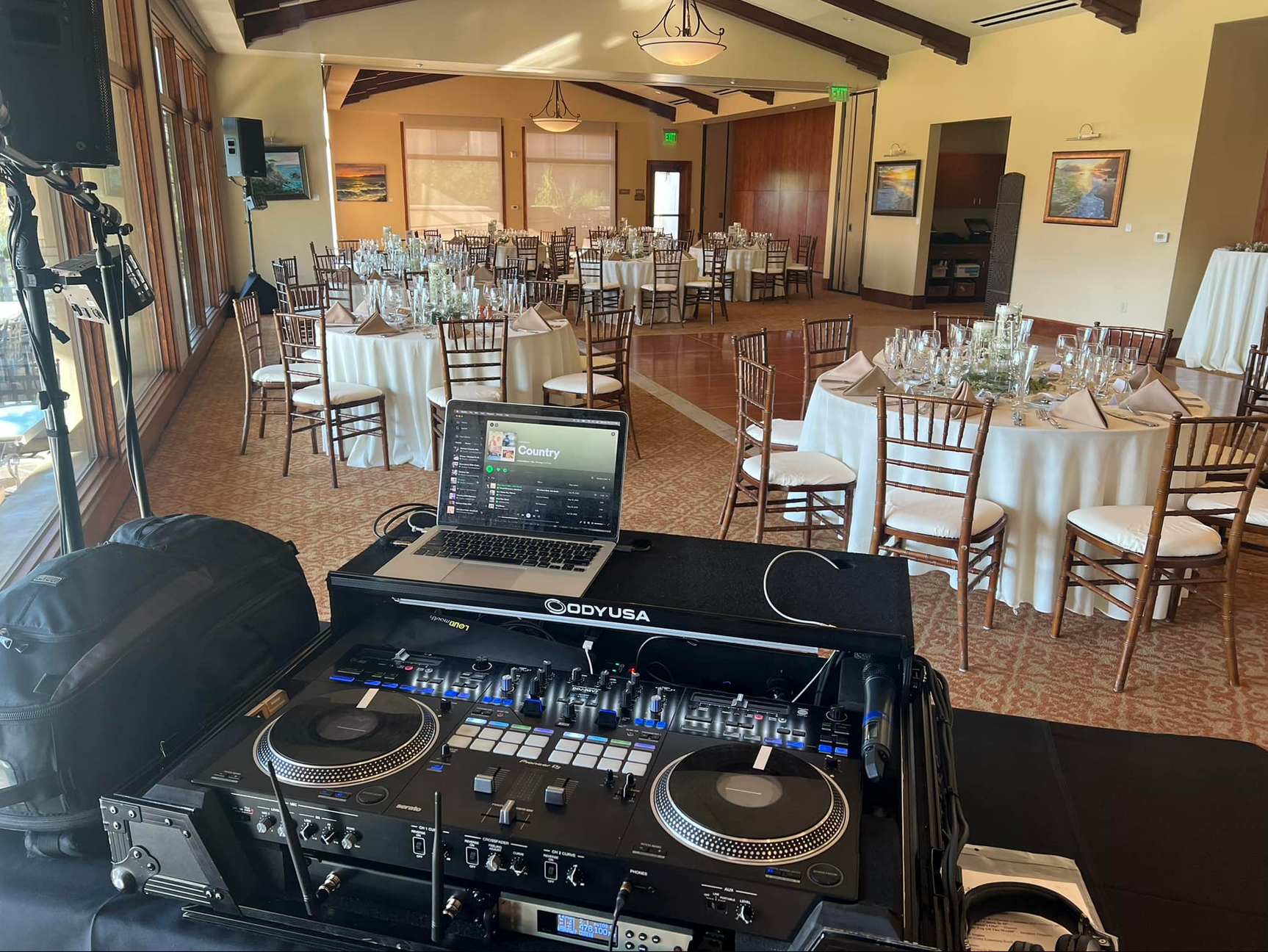 DJ setup at a wedding reception with tables set for guests in a venue.