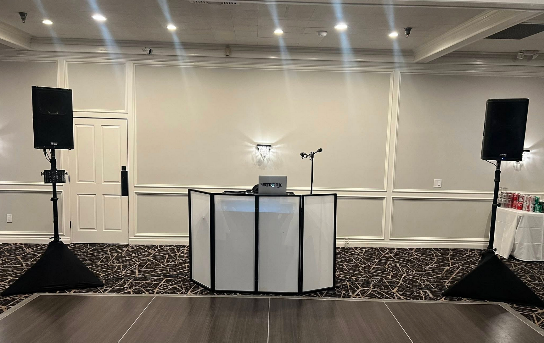 DJ setup: speakers on stands flanking a white booth with equipment, dance floor, event space.