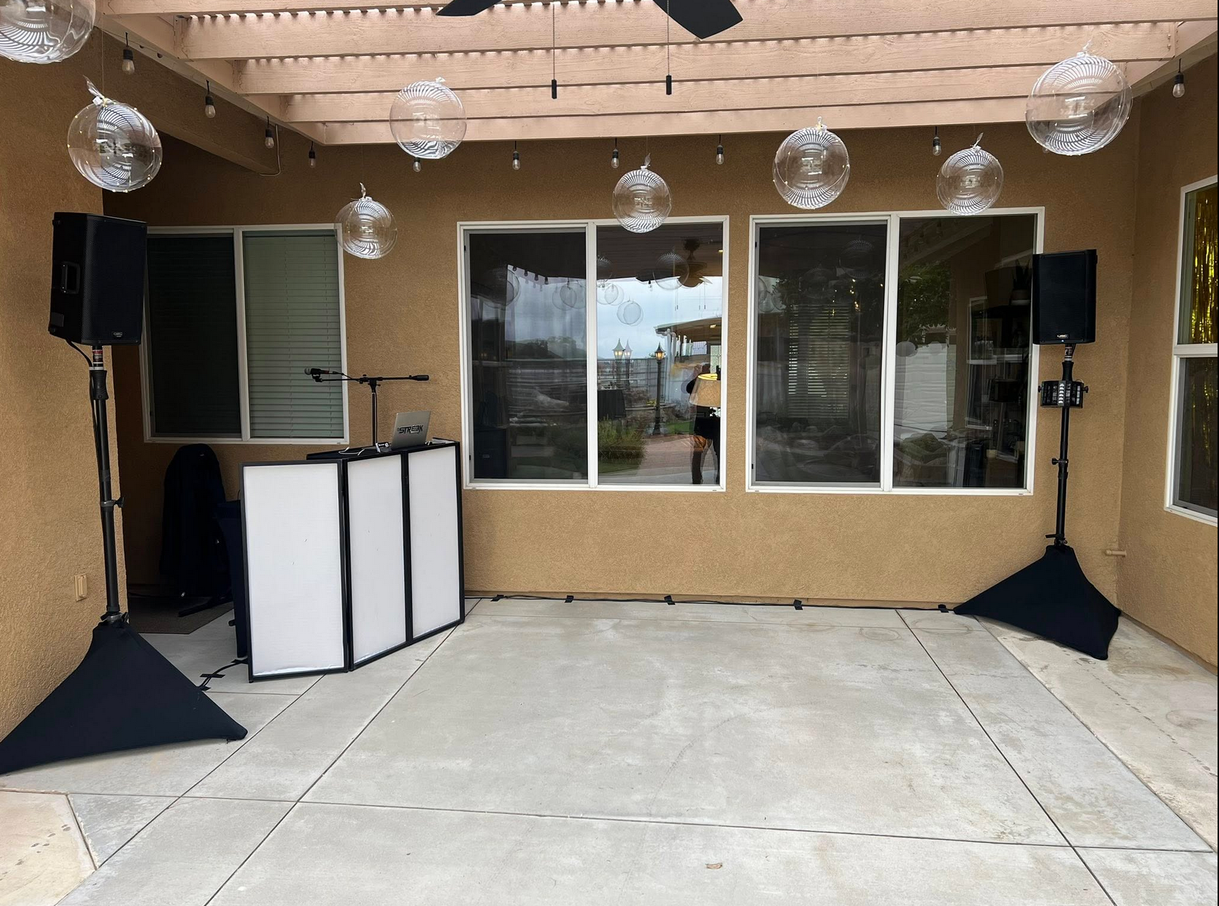Outdoor DJ setup with speakers, white panels, and decorative hanging globes.