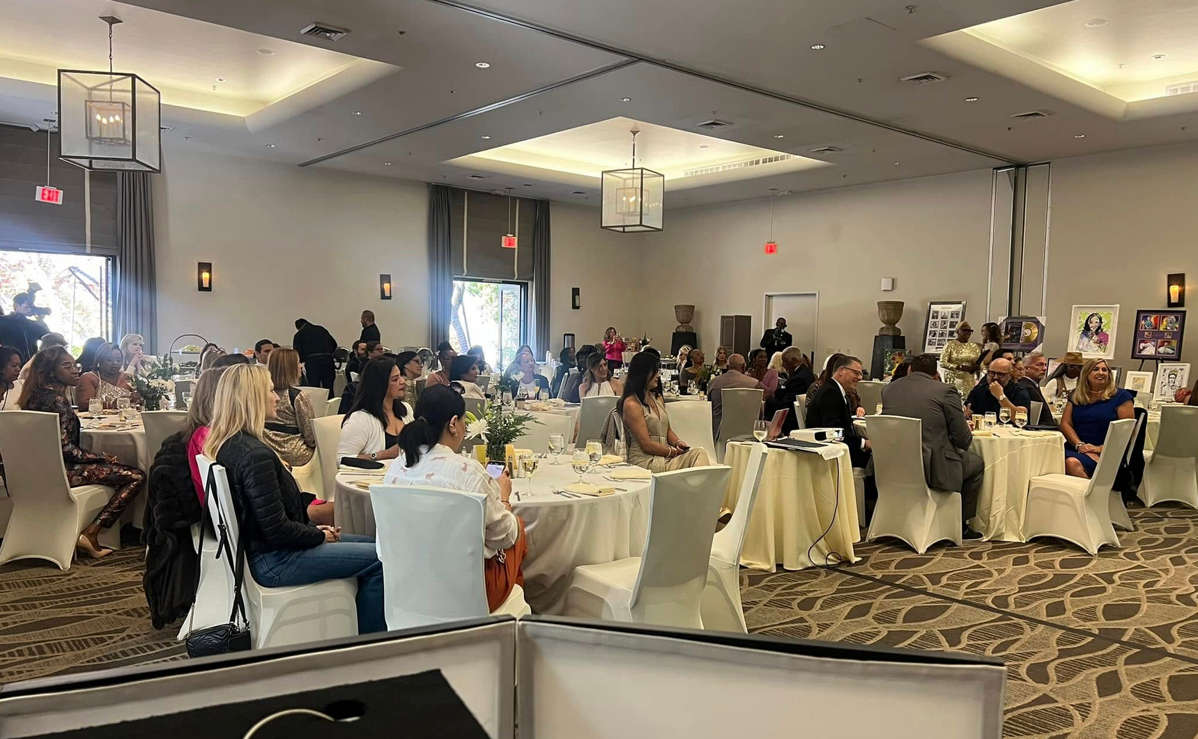 A crowded banquet hall with round tables, guests seated, and portraits on the walls.