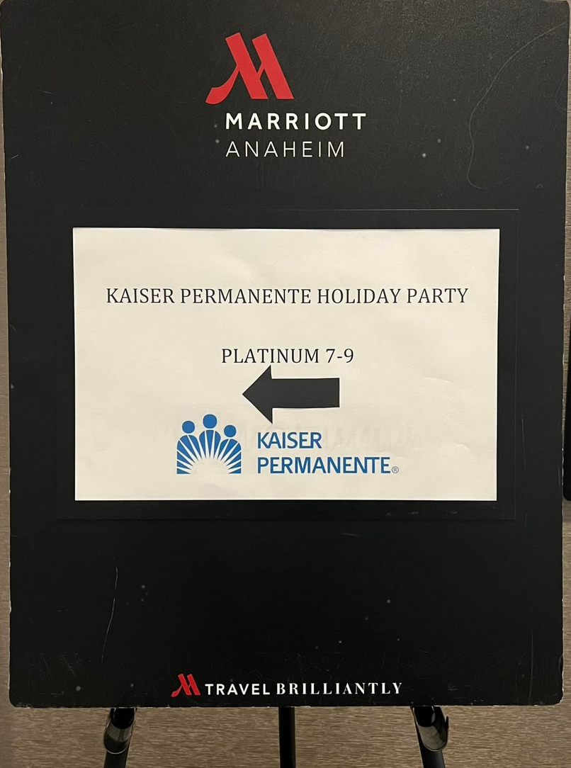 Sign for Kaiser Permanente holiday party at Marriott, black background with white text, arrow pointing left.