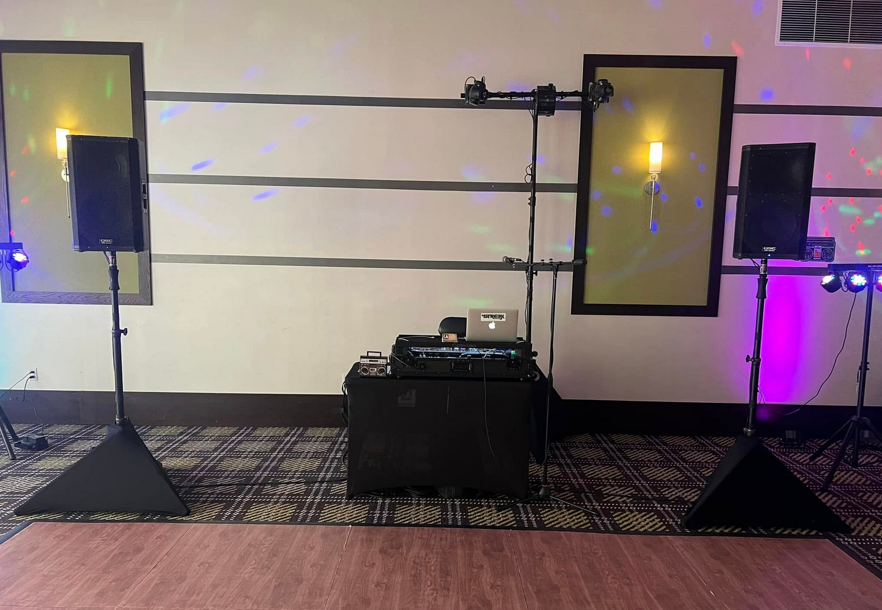 DJ setup with speakers, lights, and sound equipment on a carpeted floor against a wall.