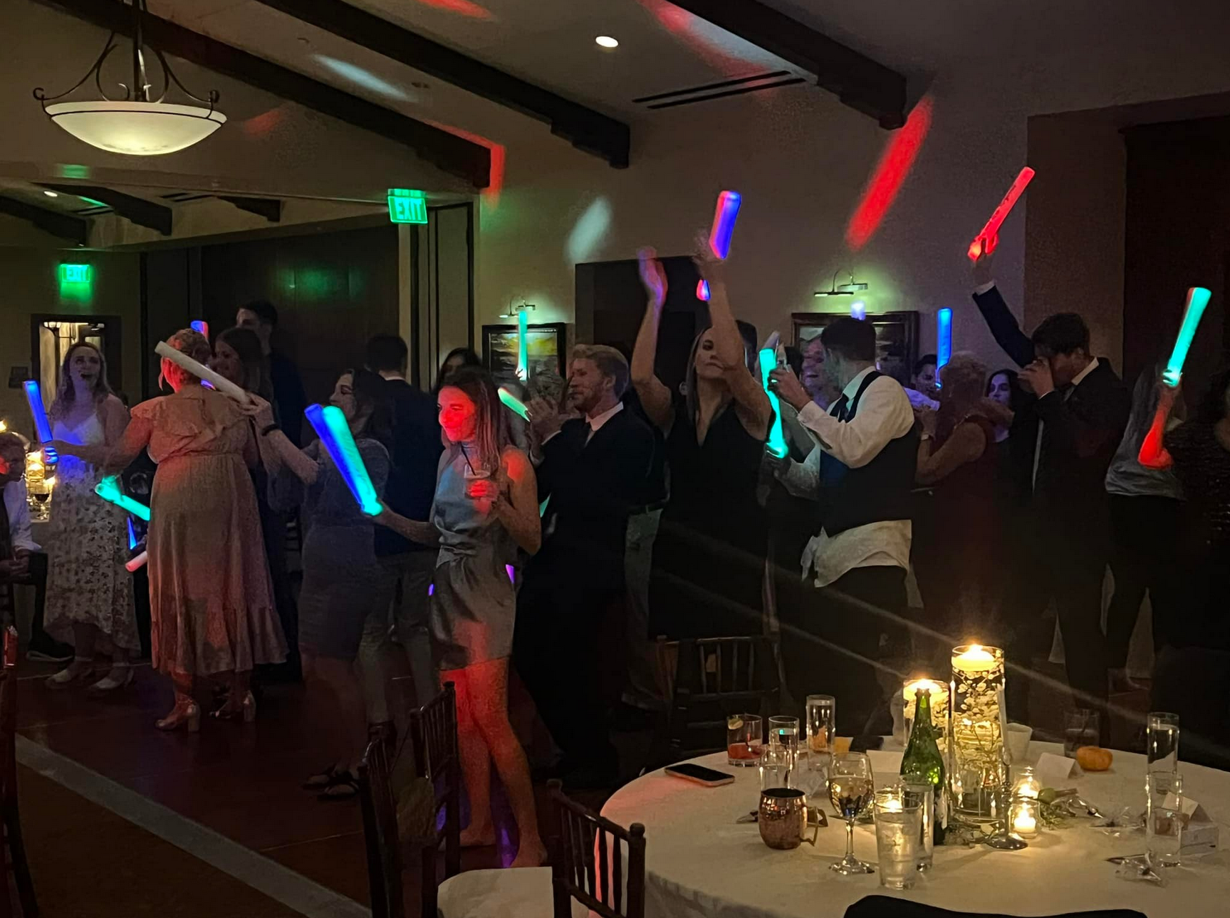 People dancing in a dimly lit room with colorful glow sticks, a celebration taking place.