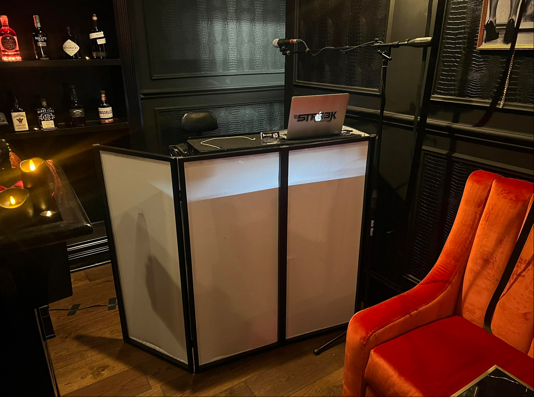 DJ setup: laptop, speakers on white and black booth, red chair in dim-lit venue.