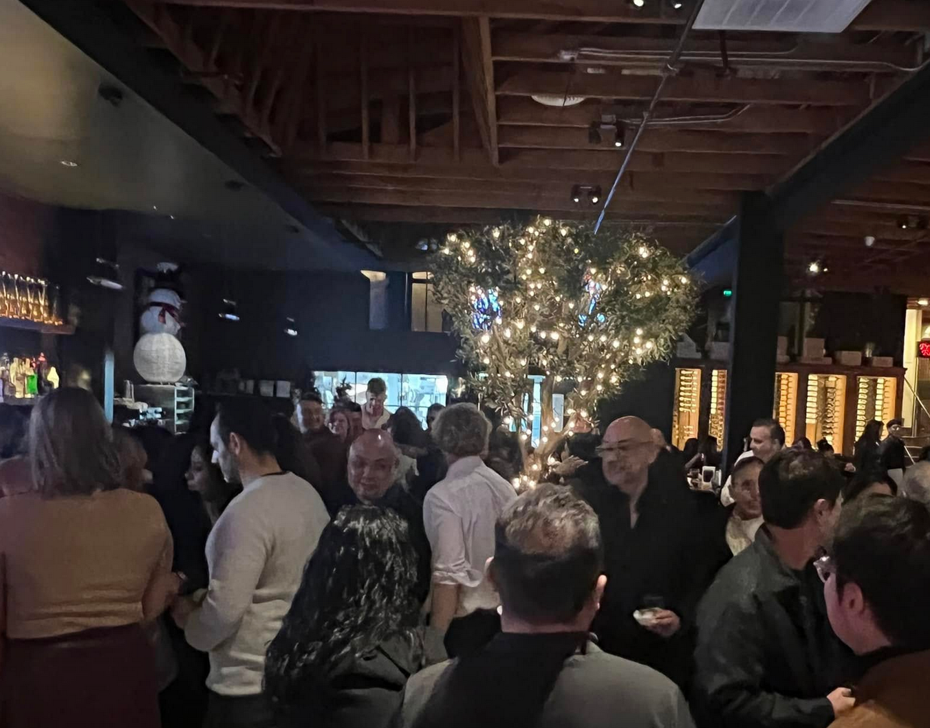 People at a crowded bar, holiday decorations, some faces visible. Dimly lit interior.
