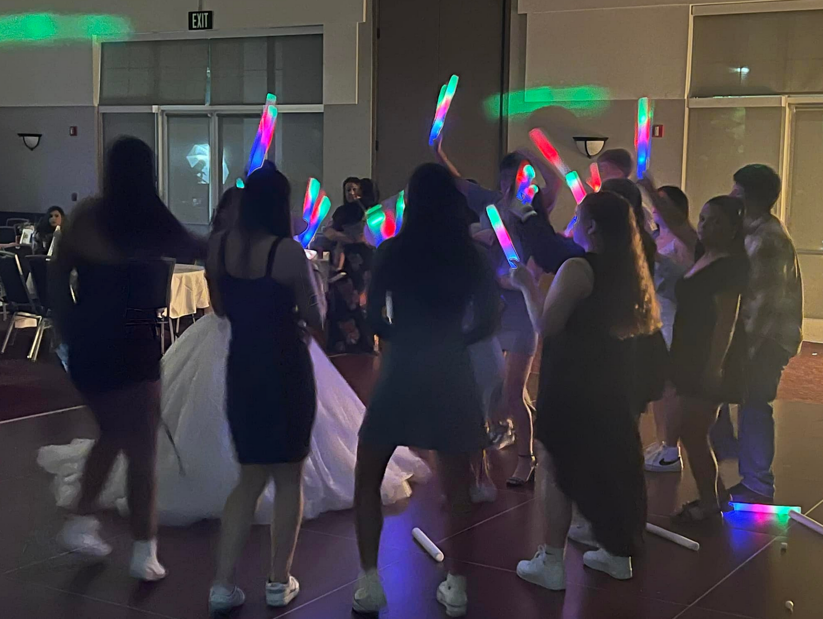 People dancing with glowing sticks in a room, some faces visible, possibly a wedding reception.