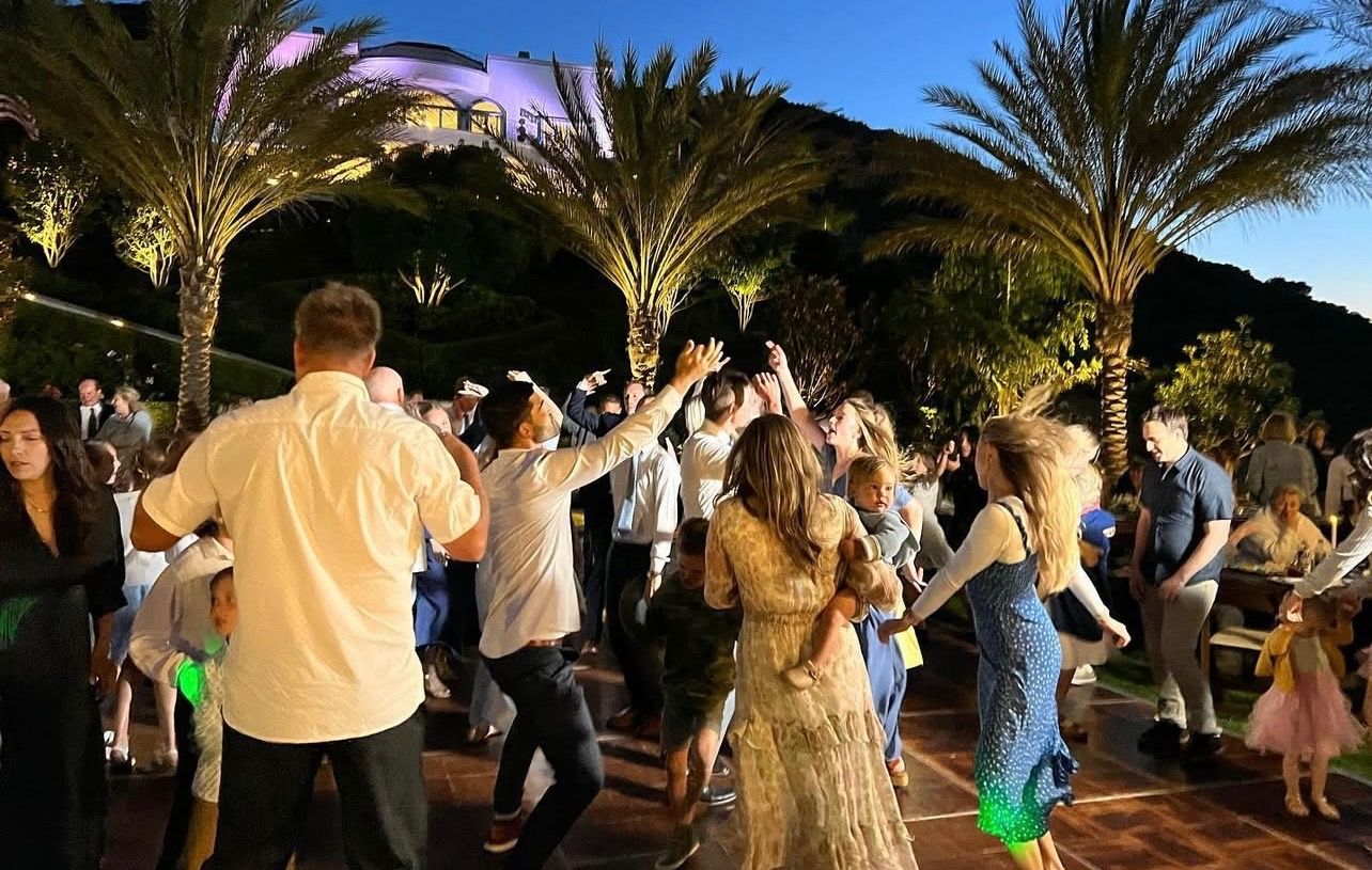 People dancing outdoors at night under palm trees.