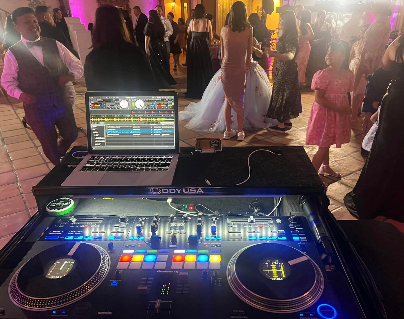 DJ setup at a wedding with a crowd dancing in the background.