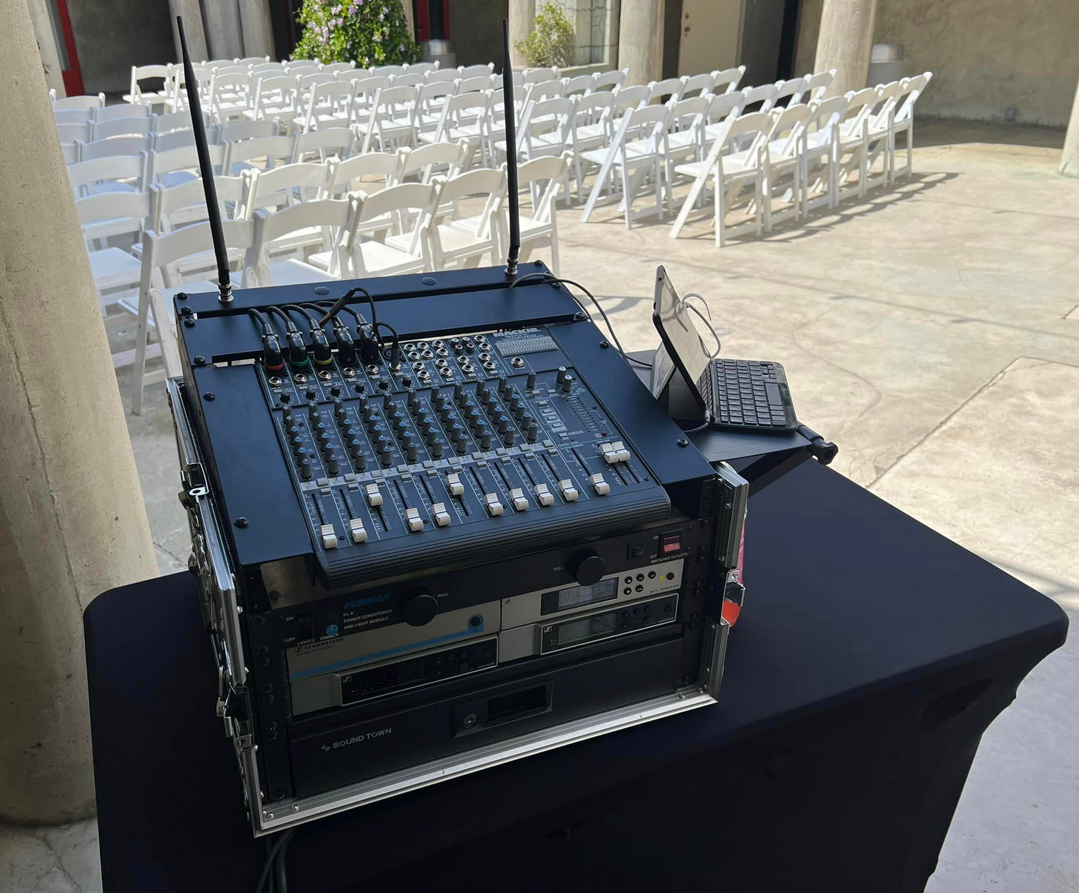 Sound mixing equipment setup outdoors before a ceremony with white chairs.