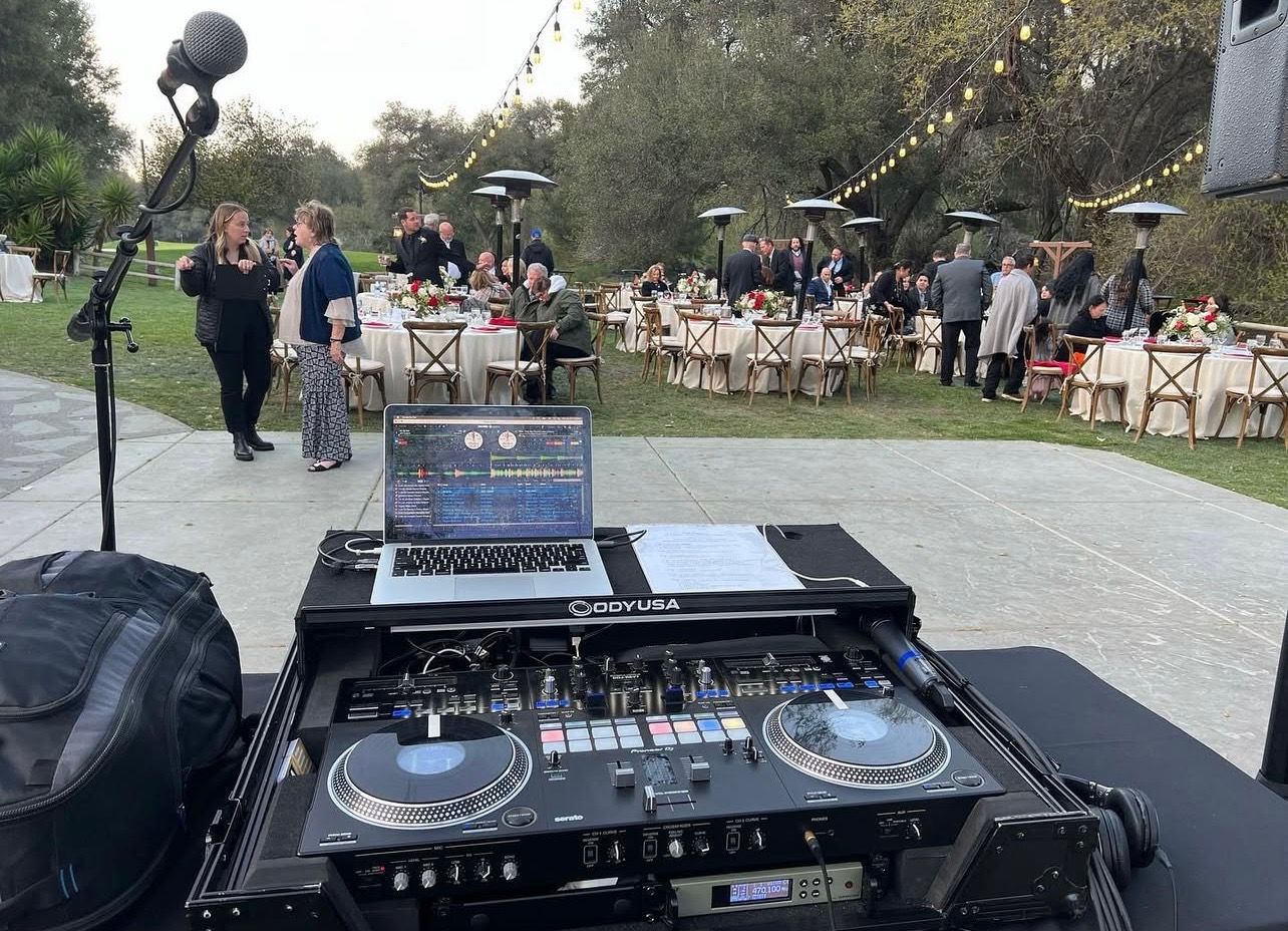 DJ setup in front of an outdoor party; guests seated at tables.