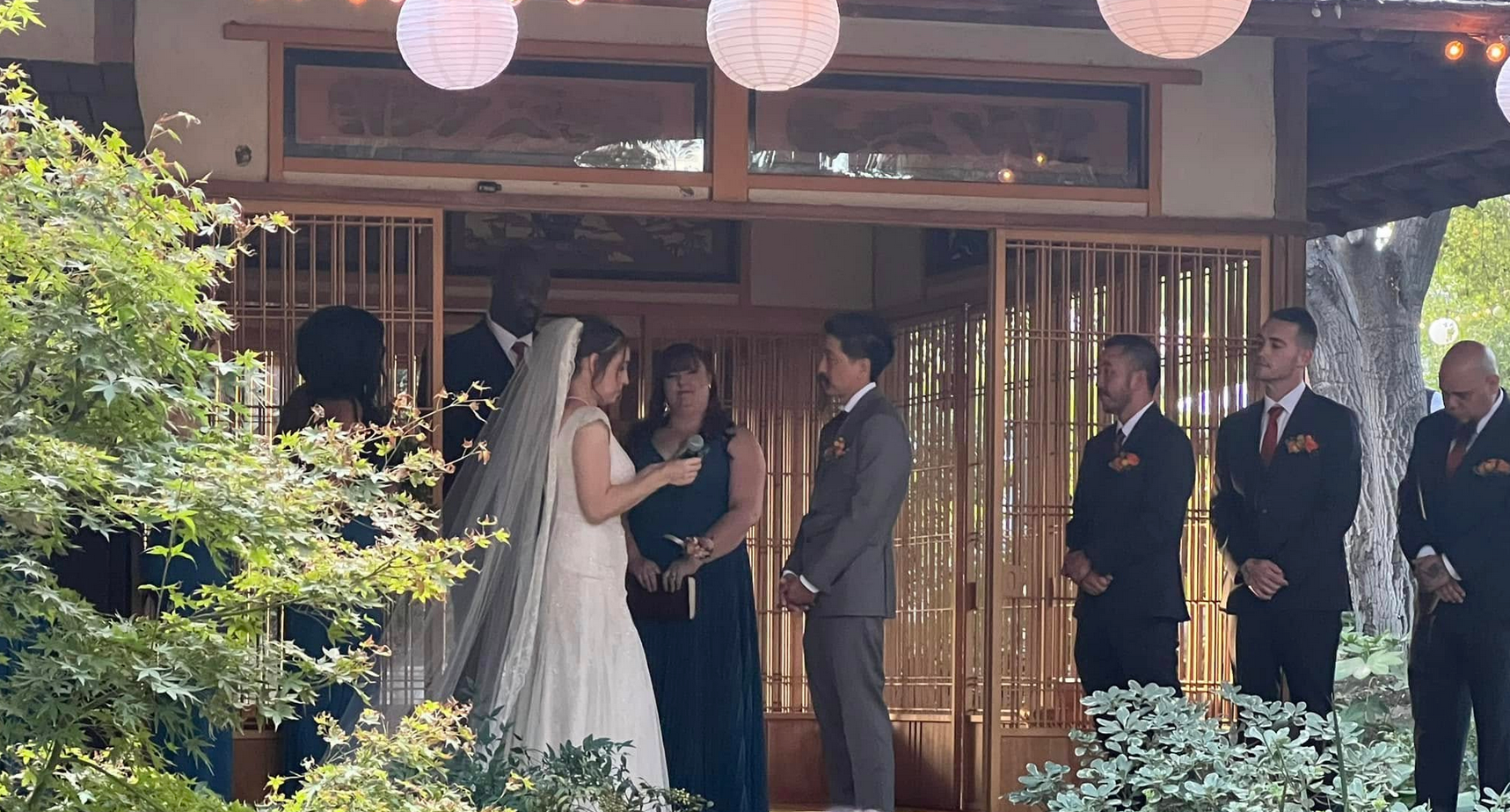 Wedding ceremony: Bride and groom at altar, officiant, attendants; outdoor setting.
