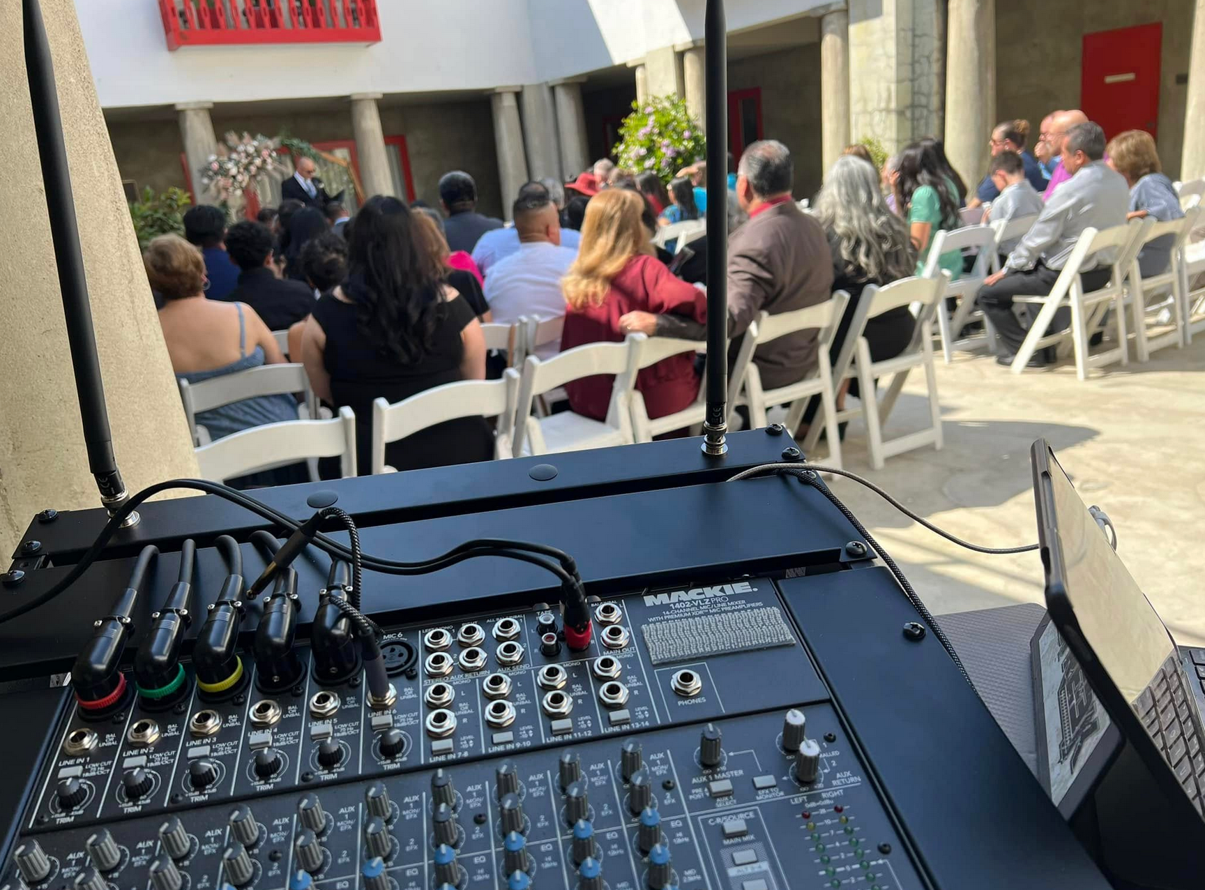 Sound mixer in front of a crowd seated at an outdoor event, red accents in background.