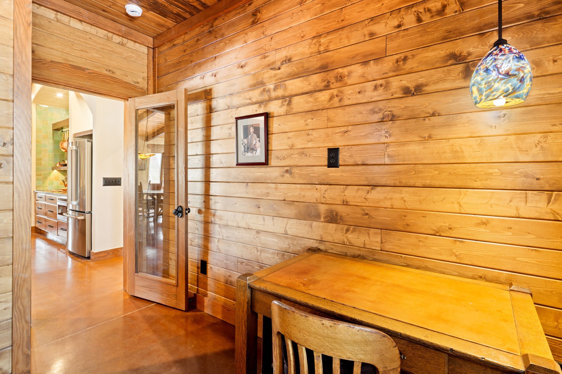 Wood-paneled hallway with glass door, small desk, and stained-glass pendant light