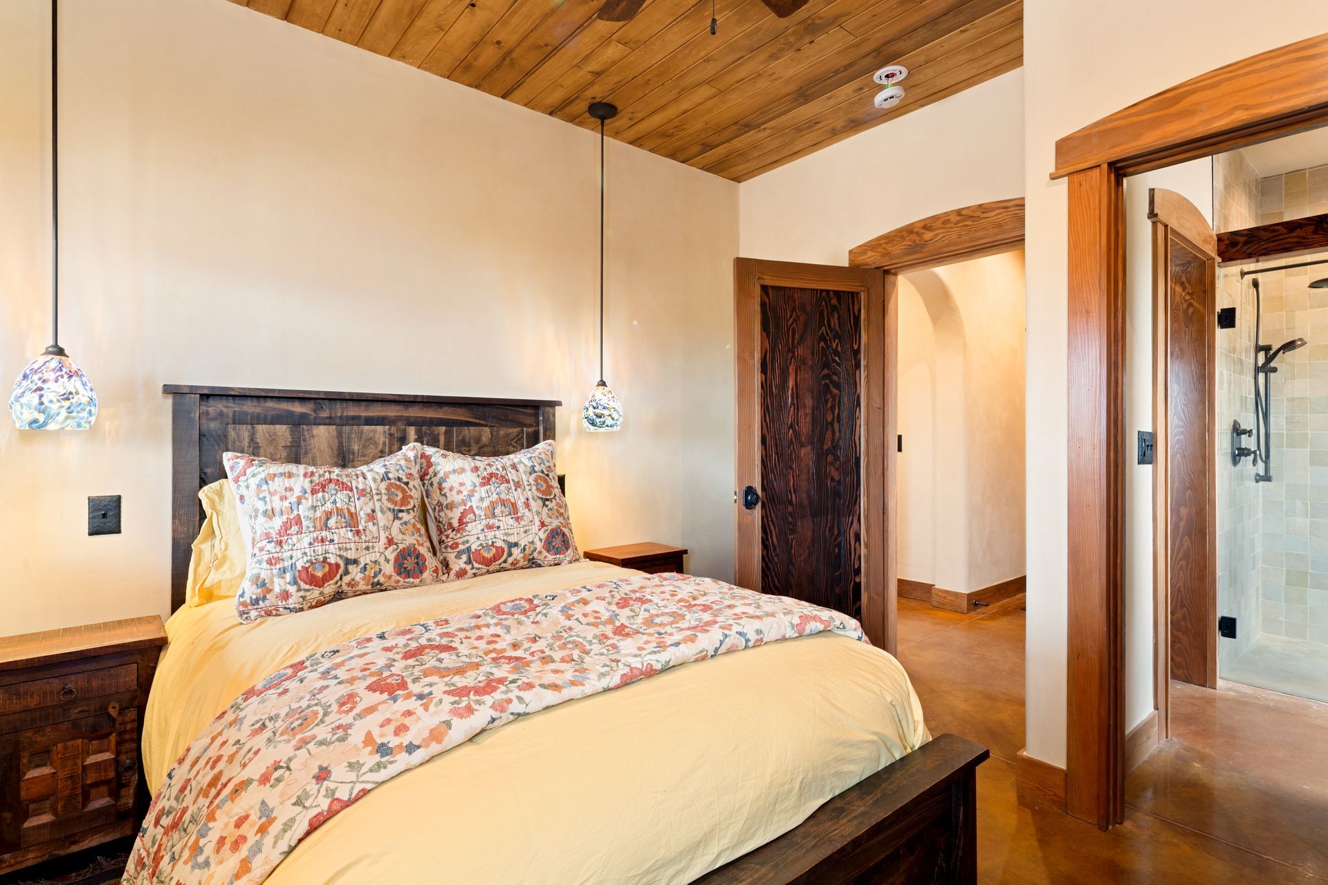 Cozy bedroom with floral bedding, wooden ceiling, and adjoining bathroom doorway