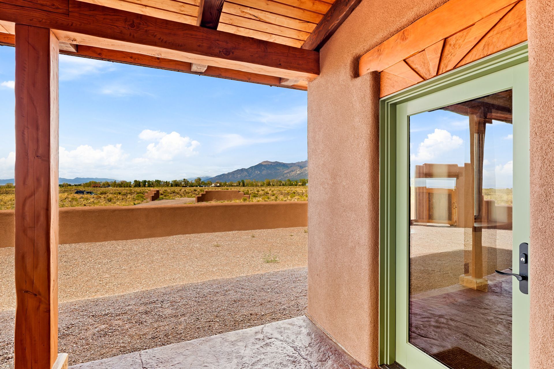 Covered patio with green-framed door, stucco wall, and desert mountain view beyond a low wall