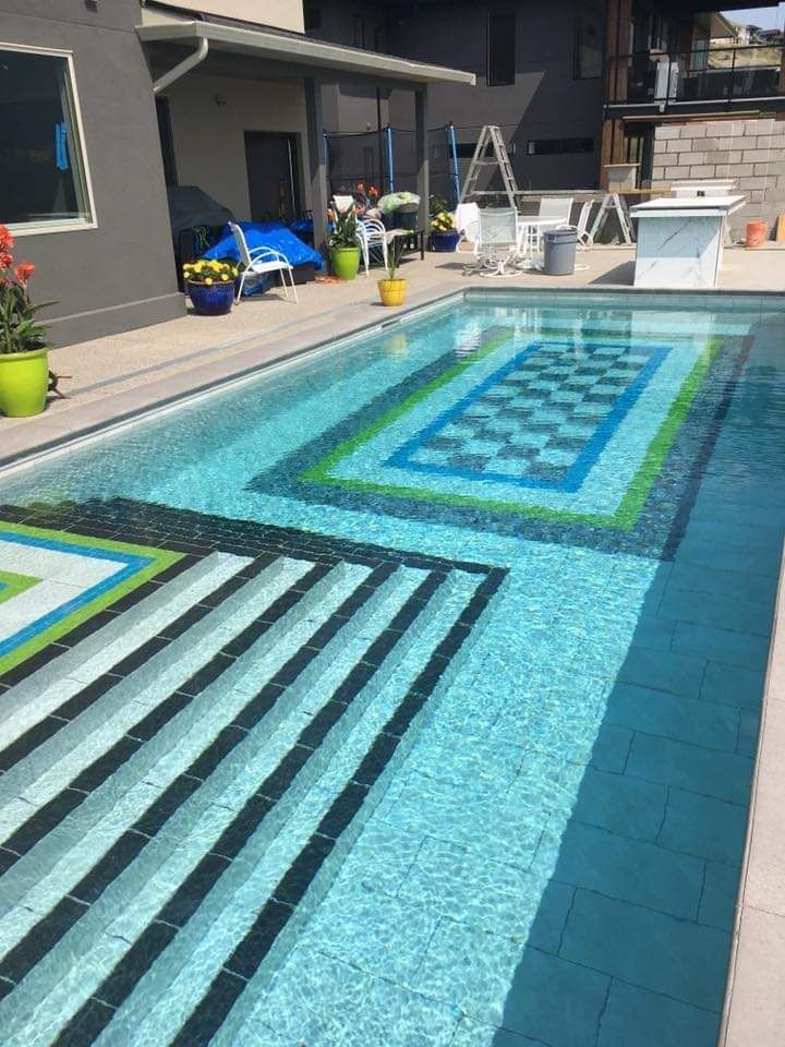 Backyard swimming pool with blue water, patterned tile inlay, and lounge chairs on the patio