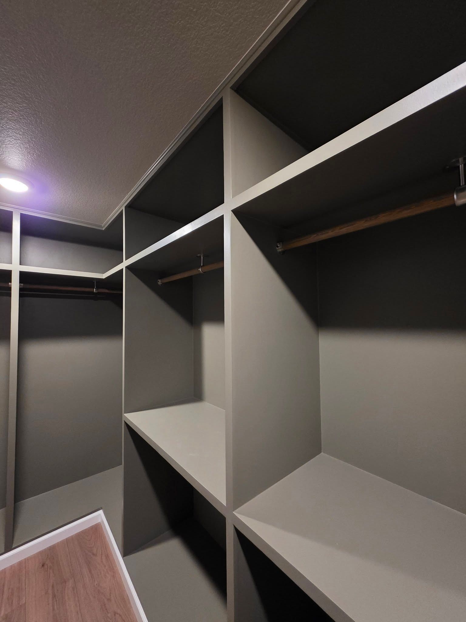 Empty gray walk-in closet with built-in shelves and hanging rods.