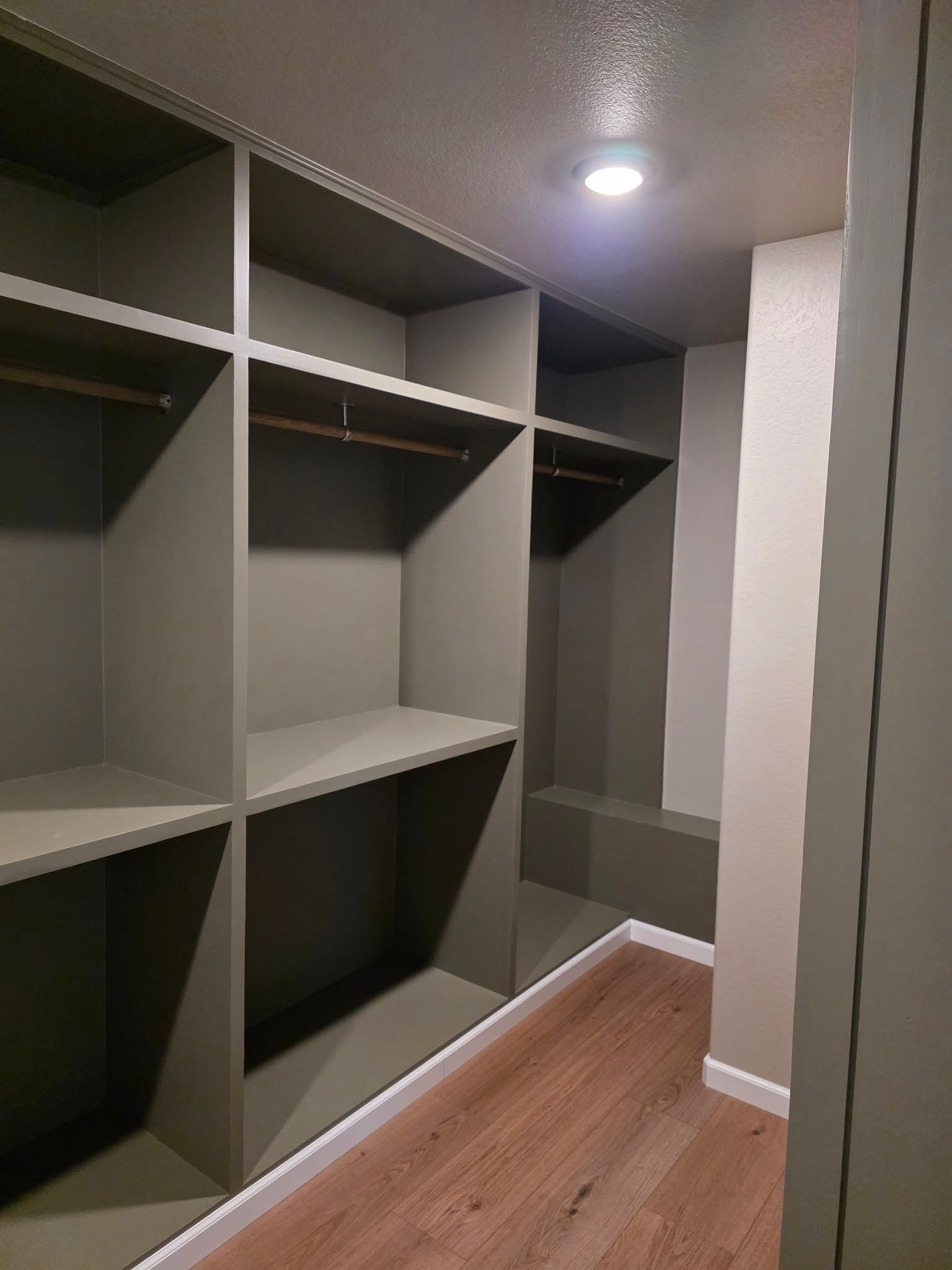 Empty walk-in closet with gray built-in shelves, hanging rods, and wood flooring.