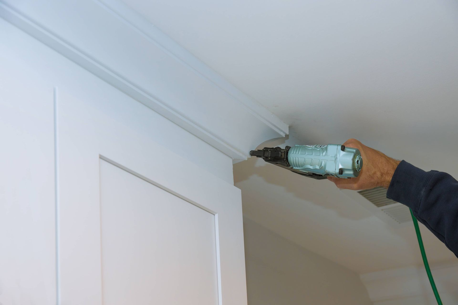 Hand holding a drill near a white ceiling molding in a room