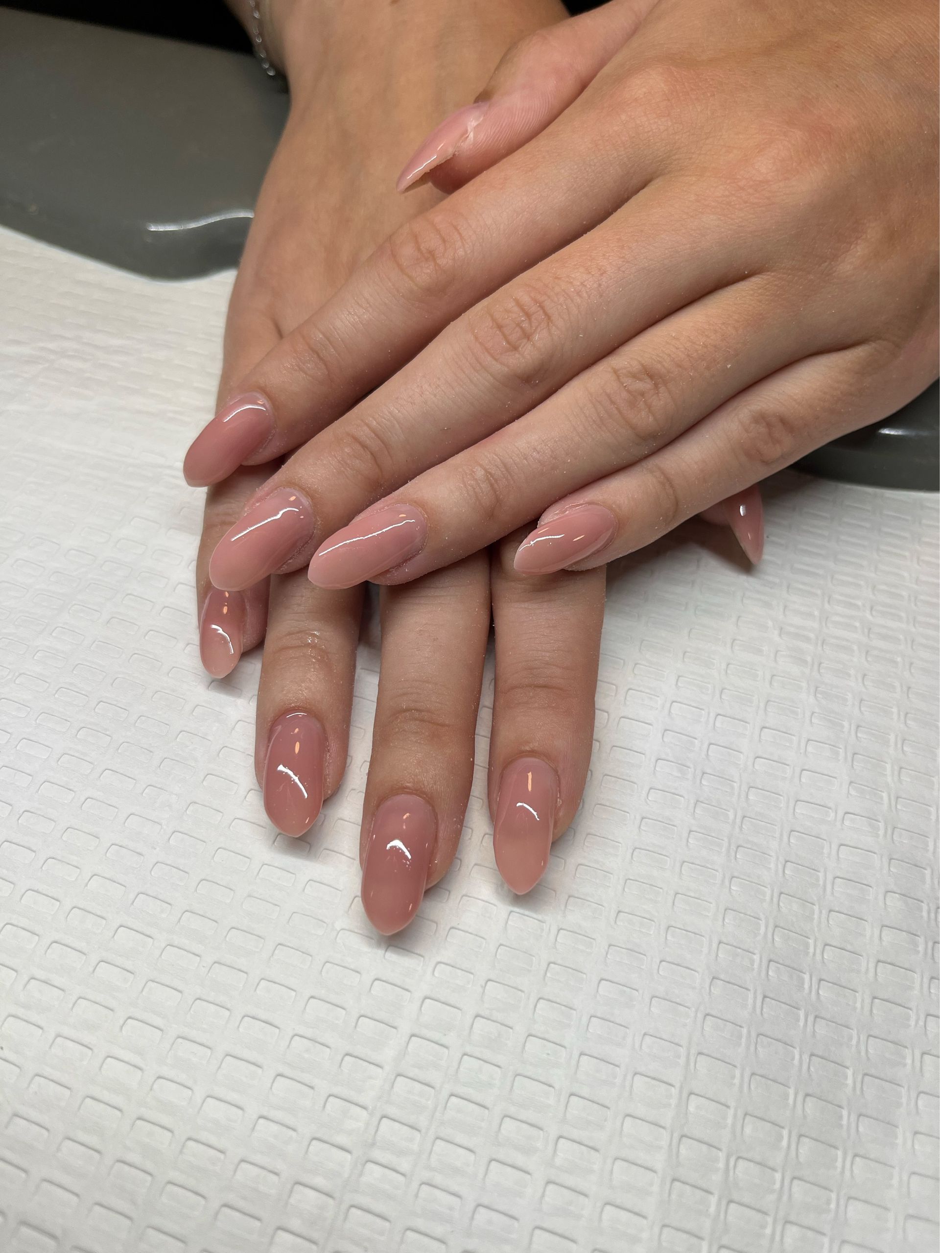 Hands with glossy pink manicure resting on a white textured towel