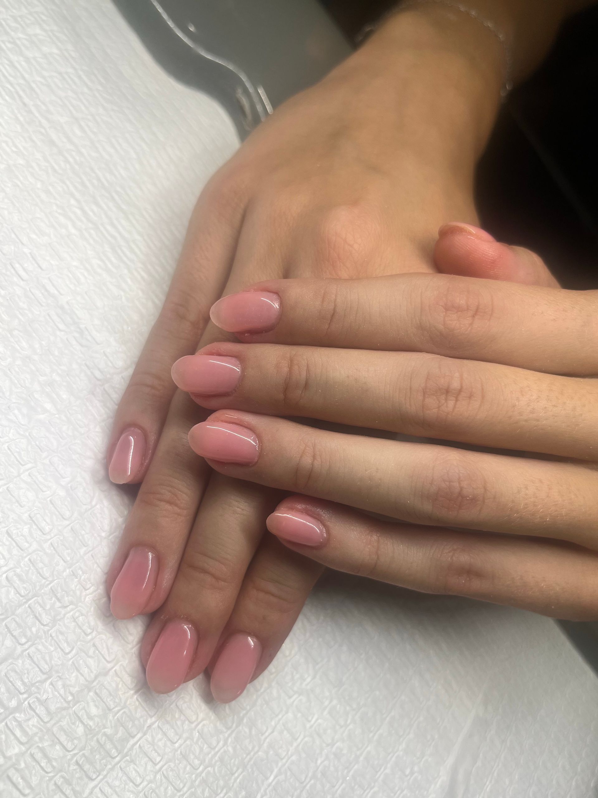 Hands with glossy pink manicured nails resting on a white towel.