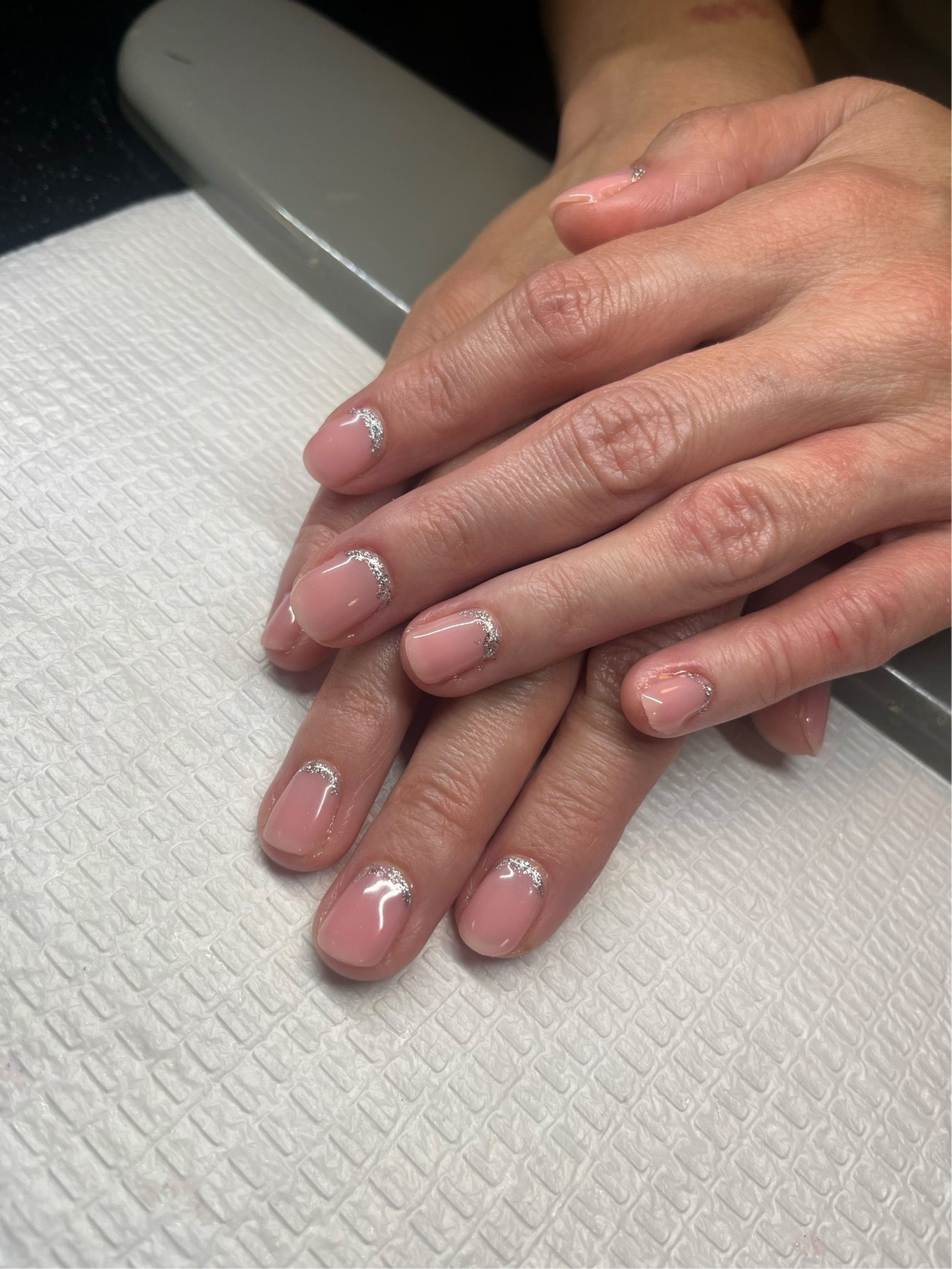 Hands with pink glitter nail polish resting on a white towel at a manicure station